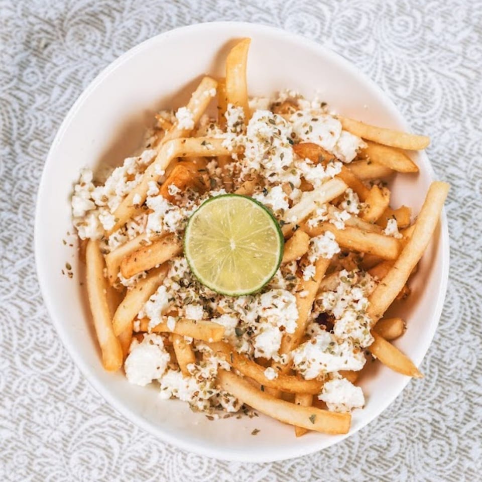 Golden french fries topped with crumbled feta cheese, dried herbs, and a lime slice in a white bowl.