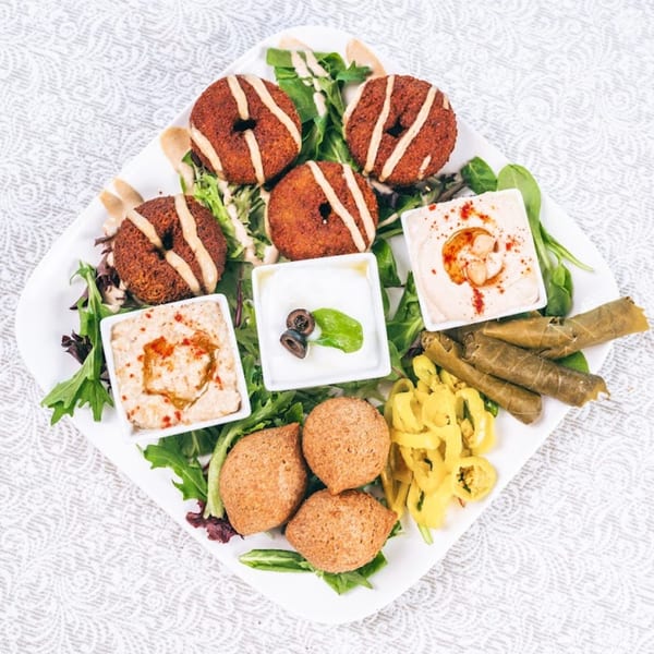 A white platter with falafel, kibbeh, stuffed grape leaves, hummus, and yogurt dip.