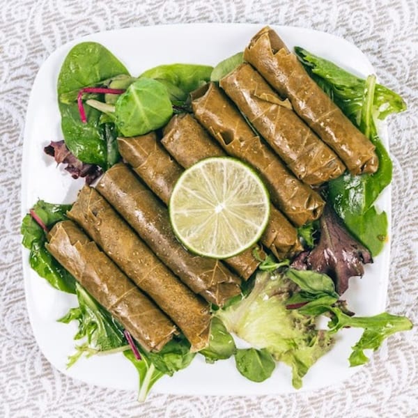 Dolmades, or stuffed grape leaves, with a lime slice and fresh greens on a white plate.