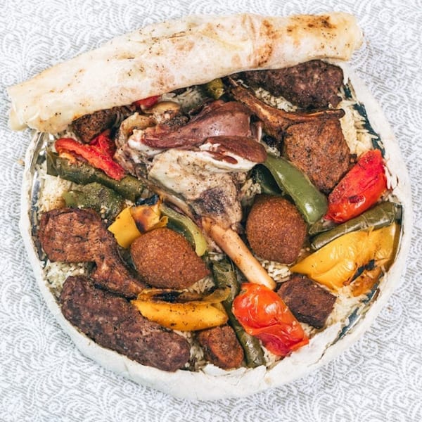A large platter of rice, various meats, roasted peppers, and kibbeh, topped with flatbread.