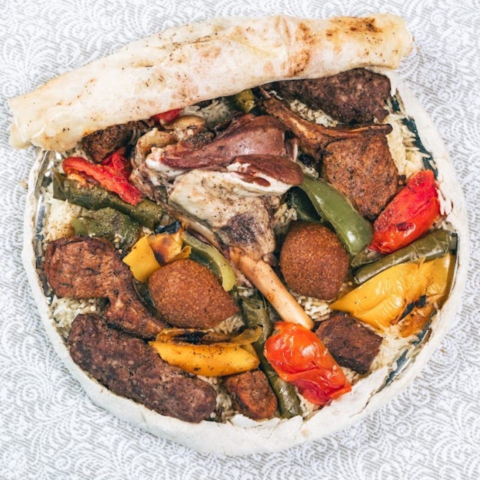 A large platter of rice, various meats, roasted peppers, and kibbeh, topped with flatbread.
