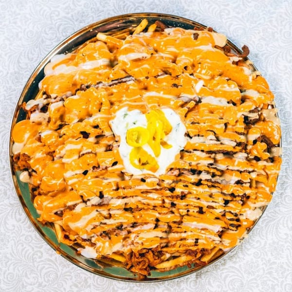 A large platter of loaded fries topped with orange cheese sauce, white sauce, and yellow peppers.