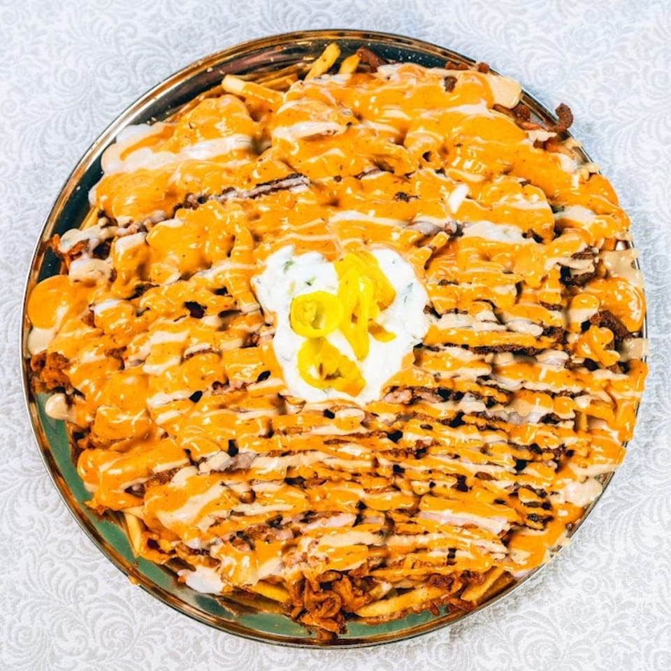 A large platter of loaded fries topped with orange cheese sauce, white sauce, and yellow peppers.