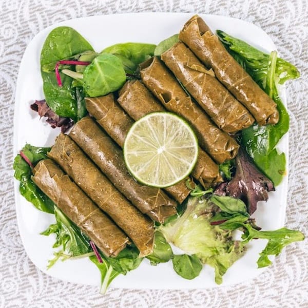 Dolmades, or stuffed grape leaves, with a lime slice and fresh greens on a white plate.