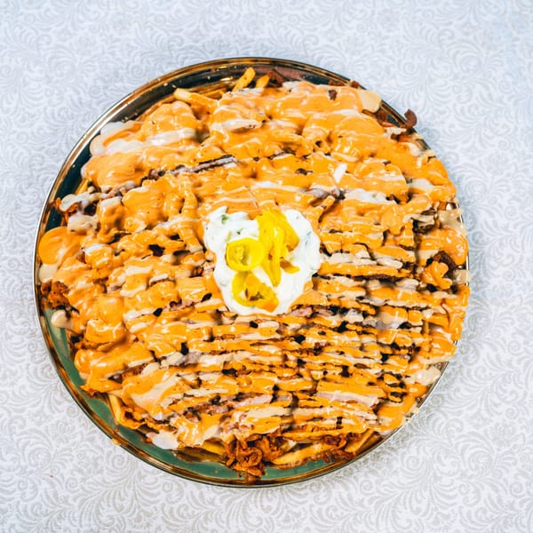 A large platter of loaded fries with orange and white sauces, topped with pickled yellow peppers.